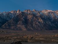 the sun sets behind a majestic mountain range in the desert, with snow on the top