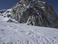 a mountain with snow covered rocks and a man on skis standing under a mountain