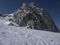 a mountain with snow covered rocks and a man on skis standing under a mountain