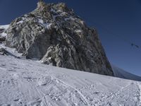 a mountain with snow covered rocks and a man on skis standing under a mountain