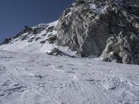 a mountain with snow covered rocks and a man on skis standing under a mountain