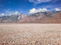 a barren plain with mountains in the distance and gravel on the ground beneath it,