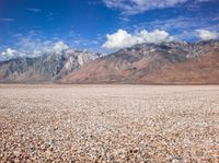 a barren plain with mountains in the distance and gravel on the ground beneath it,