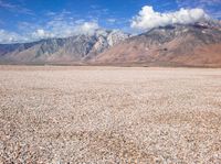 a barren plain with mountains in the distance and gravel on the ground beneath it,