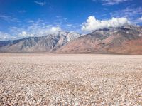 a barren plain with mountains in the distance and gravel on the ground beneath it,