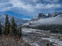 snowy mountain with a cloud covering the snow covered area above the mountains, a village and trees in the distance