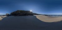 a large rock in the sand by the ocean with a setting sun behind it on a sunny day