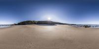 a large rock in the middle of the sand at the ocean's edge, with bright sun shining down on its