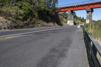 a bridge over the highway has an orange metal railing leading to it and people walking on the side