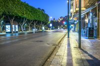 a long street with lights at night in the city with trees lining the curb,