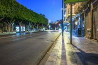 a long street with lights at night in the city with trees lining the curb,