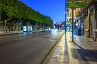 a long street with lights at night in the city with trees lining the curb,