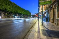 a long street with lights at night in the city with trees lining the curb,