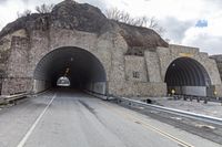 a tunnel that has cars in it near the side of the road with a rock formation