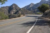 a street in the middle of a mountainside with a mountain range and yellow stripe lines