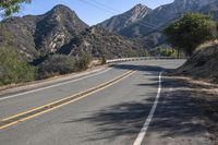 a street in the middle of a mountainside with a mountain range and yellow stripe lines