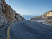 a motorcycle that is on a curved road near a large cliff with the water in the distance