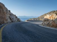 a motorcycle that is on a curved road near a large cliff with the water in the distance