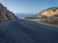 a motorcycle that is on a curved road near a large cliff with the water in the distance