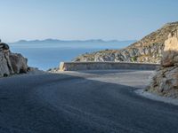 a motorcycle that is on a curved road near a large cliff with the water in the distance