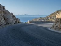 a motorcycle that is on a curved road near a large cliff with the water in the distance