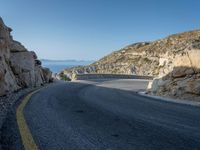 a motorcycle that is on a curved road near a large cliff with the water in the distance