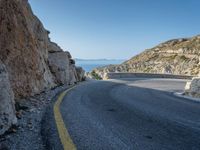 a motorcycle that is on a curved road near a large cliff with the water in the distance