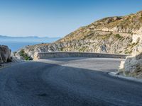 a motorcycle that is on a curved road near a large cliff with the water in the distance