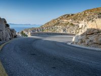 a motorcycle that is on a curved road near a large cliff with the water in the distance