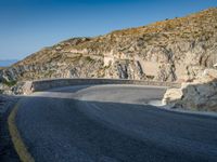 a motorcycle that is on a curved road near a large cliff with the water in the distance