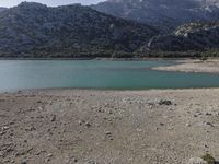 a mountain range and a body of water surrounded by green grass and rocks is shown