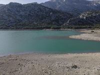 a mountain range and a body of water surrounded by green grass and rocks is shown