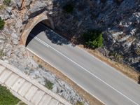 there is a long curved road next to the wall in the mountains under which is a road going under it