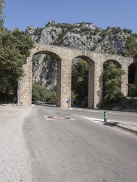 a road that is lined with arches near trees and some rocks on the side of the street