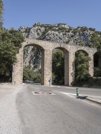 a road that is lined with arches near trees and some rocks on the side of the street