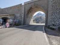 a street with stone archway on side of it with buildings in background and mountains in the distance