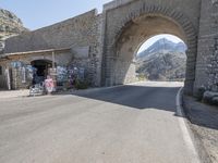 a street with stone archway on side of it with buildings in background and mountains in the distance