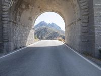 a stone arch over an empty road with mountains and hills in the background the sky is clear and blue