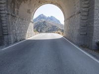 a stone arch over an empty road with mountains and hills in the background the sky is clear and blue