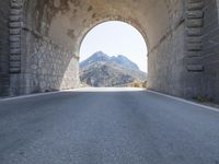 a stone arch over an empty road with mountains and hills in the background the sky is clear and blue