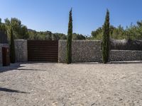 a gravel driveway and fence surrounding it in the daytime sun, with stone walls surrounding