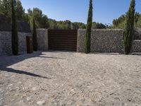 a gravel driveway and fence surrounding it in the daytime sun, with stone walls surrounding