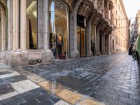 people in the street with clothes in store front window display windows and cobbles on either side