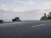 a small gray motorcycle driving on a road next to the ocean, next to a tower