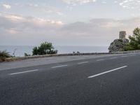 a small gray motorcycle driving on a road next to the ocean, next to a tower