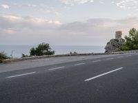 a small gray motorcycle driving on a road next to the ocean, next to a tower