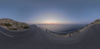 a curved road on top of an island with the sun setting over the water in the background