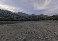 the view over the water of the valley from where the shore meet the mountains, with sparse vegetation and small stones all around