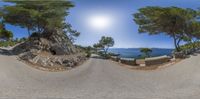 a street with rocks, trees and a rock formation behind it with a blue sky