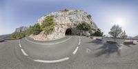 an empty highway near a rocky outcropping and blue sky above it that has a tunnel on top of it